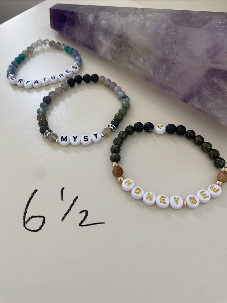 May include: Three beaded bracelets with white letter beads spelling "CREATURES", "MYST", and "HONEYBEE". The bracelets are made with various colored stones and beads. The size is written as 6 1/2 inches.