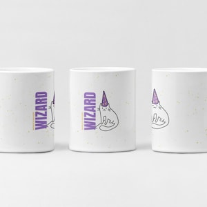 Könnte beinhalten: Weiße Keramiktasse mit einer Illustration einer Katze mit Zaubererhut und dem Wort "WIZARD" in Lila. Die Tasse hat einen Henkel und ein gesprenkeltes Design. Die Katze trägt einen lila Zaubererhut.