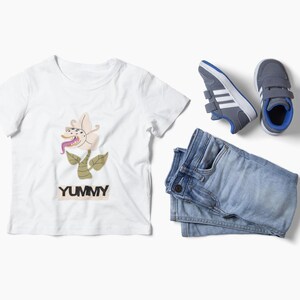 Puede incluir: Una camiseta blanca con un gráfico de flores y la palabra "YUMMY". La imagen también incluye vaqueros azules y zapatillas grises con rayas blancas y detalles azules. La ropa es para niños.