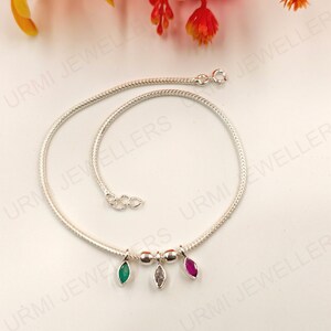 Könnte beinhalten: Ein silbernes Ketten-Fußkettchen mit einem feinen Schlangenkettendesign und einem Karabinerverschluss. Das Fußkettchen ist mit drei kleinen, marquise-geschliffenen Anhängern in Grün, Transparent und Pink verziert, die durch zwei kleine Silberperlen getrennt sind.