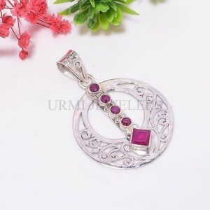 May include: A silver pendant with a circular filigree design. The pendant features a row of five round, dark pink gemstones and a square gemstone. The pendant has a loop for a chain.