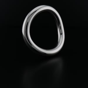 May include: A polished, silver-toned ring with a continuous, flowing design. The ring's surface reflects light, creating highlights and shadows against a black background. The ring's shape is a continuous loop, suggesting a modern, minimalist aesthetic.