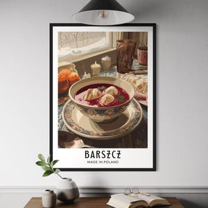 Könnte beinhalten: Gerahmter Kunstdruck mit einer Schüssel roter Borschtsch-Suppe mit Knödeln, auf einem Tisch mit anderen Gerichten und einem Blick aus dem Fenster. Der Druck hat das Wort "BARSZCZ" und "MADE IN POLAND" in weißer Schrift.