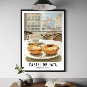 May include: Framed print depicting a cafe scene with two pastel de nata pastries on a plate, a cup of coffee, and a cityscape. The text "PASTEL DE NATA MADE IN PORTUGAL" is displayed below the image.