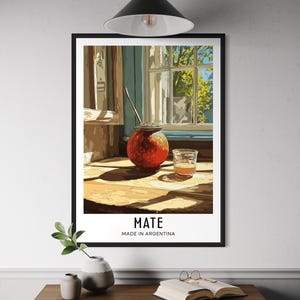Peut inclure: Impression d'art encadrée représentant une nature morte d'une boisson mate argentine traditionnelle. L'image montre une gourde rouge avec une paille métallique, un verre de jus et le texte "MATE MADE IN ARGENTINA". La scène est située près d'une fenêtre.