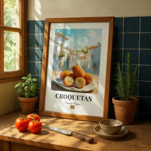 May include: A framed wall art print featuring a painting of golden-brown croquettes on a plate with a Spanish village background. The text reads CROQUETAS Flavours of Spain with a small Spanish flag icon centred below the main title.