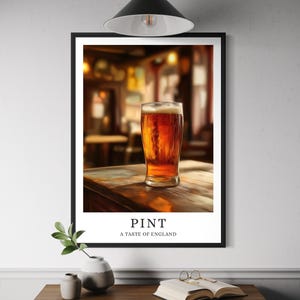 May include: A framed print showing a pint of amber beer in a glass, with the text "PINT" and "A TASTE OF ENGLAND". The background is a blurred pub scene. The print is mounted on a wall above a wooden table.