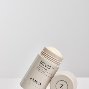 K&ouml;nnte beinhalten: Ein wei&szlig;er und beiger feuchtigkeitsspendender Fersenbalsam-Stick mit dem Text "Moisturizing Heel Balm Intensive Therapy 1.5 OZ / 71 GM" und dem Markennamen "ZAVINA" auf der Seite. Die Unterseite des Sticks hat ein Etikett mit dem Buchstaben "Z" und dem Text "Made with clean ingredients - Made with clean ingredients".