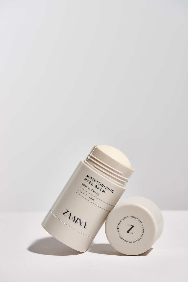 K&ouml;nnte beinhalten: Ein wei&szlig;er und beiger feuchtigkeitsspendender Fersenbalsam-Stick mit dem Text "Moisturizing Heel Balm Intensive Therapy 1.5 OZ / 71 GM" und dem Markennamen "ZAVINA" auf der Seite. Die Unterseite des Sticks hat ein Etikett mit dem Buchstaben "Z" und dem Text "Made with clean ingredients - Made with clean ingredients".
