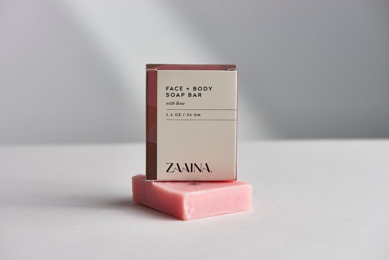 K&ouml;nnte beinhalten: Eine rosa Seifenstange mit dem Text "FACE + BODY SOAP BAR with Rose 1.2 OZ / 34 GM ZAMINA." auf der Verpackung.