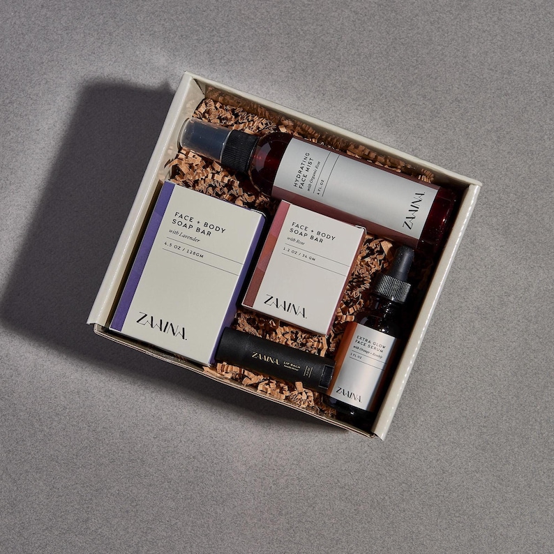 May include: A gift set containing skincare products. The set includes a face mist, face serum, and face and body soap bars. The products are packaged in a white box with brown filler. The brand name "ZAAINA" is visible on the products.