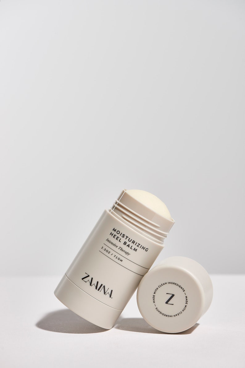 Puede incluir: Un stick de b&aacute;lsamo hidratante para los talones de color blanco y beige con el texto "Moisturizing Heel Balm Intensive Therapy 1.5 OZ / 71 GM" y el nombre de la marca "ZAVINA" impreso en el lateral. La parte inferior del stick tiene una etiqueta con la letra "Z" y el texto "Made with clean ingredients - Made with clean ingredients".