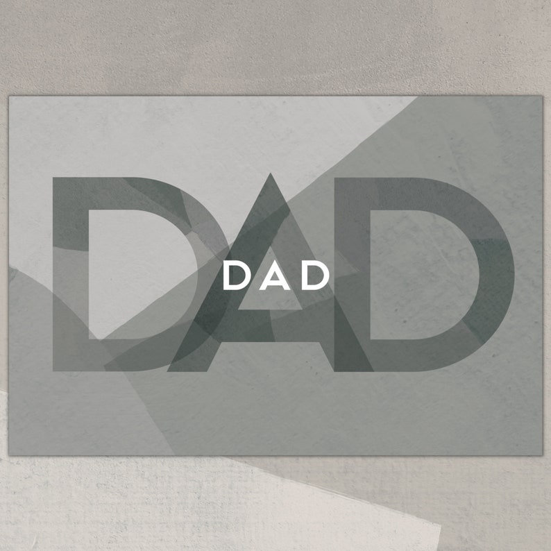 Op de afbeelding: Een grijze en witte kaart met het woord "DAD" in grote, vetgedrukte, zwarte letters. De letters zijn gelegd over een geometrisch patroon van grijze driehoeken.