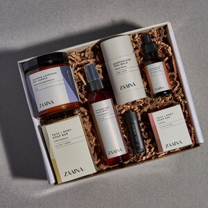 K&ouml;nnte beinhalten: Eine Geschenkbox gef&uuml;llt mit einer Auswahl an K&ouml;rperpflegeprodukten, darunter eine Kerze, ein Gesichtsnebel, eine K&ouml;rpercreme, ein Lippenbalsam und eine Seife. Die Produkte stammen alle von der Marke "ZAINA" und sind in einer wei&szlig;en Box mit braunem F&uuml;llpapier verpackt.