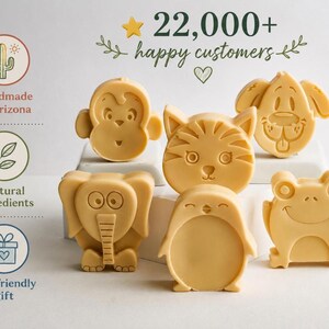 May include: Six light yellow animal-shaped soaps featuring a monkey, cat, dog, elephant, penguin, and frog. The text 22,000+ happy customers is displayed at the top, with icons for handmade in Arizona, natural ingredients, and kid-friendly gift.