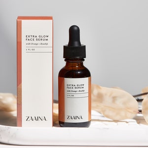 K&ouml;nnte beinhalten: Eine braune Glasflasche mit schwarzem Tropfer und einem wei&szlig;en Etikett mit der Aufschrift "EXTRA GLOW FACE SERUM with Orange + Rosehip 1 FL OZ ZAAINA."