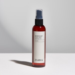 Puede incluir: Una botella de vidrio marr&oacute;n con una boquilla de pulverizaci&oacute;n negra y una etiqueta blanca que dice "Hydrating Face Mist with Organic Rose 4 FL OZ ZAINA."