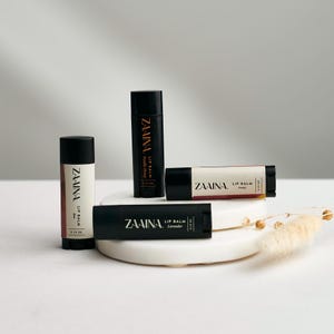 May include: Four black lip balm tubes with gold lettering. The lip balms are labeled "ZAAINA LIP BALM" with the flavors "Vanilla Honey", "Cherry", "Lavender", and "Honey".