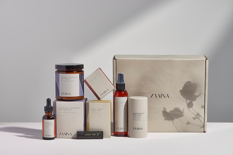 K&ouml;nnte beinhalten: Ein Geschenkkarton mit einer Auswahl an Bade- und K&ouml;rperpflegeprodukten. Das Set enth&auml;lt eine Sojawachskerze, eine Gesichts- und K&ouml;rperseife, eine feuchtigkeitsspendende Gel-Balsam, ein Gesichts-Serum und einen Lippenbalsam. Alle Produkte sind mit dem Markennamen "ZAINA" gekennzeichnet.