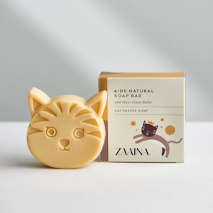 May include: A yellow cat-shaped soap bar with a brown box that says "Kids Natural Soap Bar with Shea + Cocoa Butter Cat Shaped Soap ZAAINA."