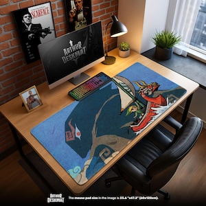 May include: A large blue desk mat with a design of a character sailing on a red boat. The desk mat measures 60cm x 120cm and has the text "ARTHUR DESKMAT". A computer, keyboard, and other items are on the desk, which is made of wood.