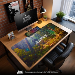May include: A large desk mat with a forest scene design, featuring trees and a mystical atmosphere. The mat is rectangular, measuring 23.6" x 47.2". The text "ARTHUR DESKMAT" is visible. A computer, keyboard, and other desk accessories are on the wooden desk.