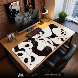 May include: A desk mat with a repeating pattern of black and white panda faces. The mat is rectangular and sits on a wooden desk, with a keyboard and monitor on top. The text "ARTHUR DESKMAT" is visible. The mouse pad size is 60cm x 120cm.
