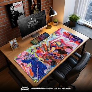 Pode incluir: Um grande tapete de rato retangular com uma vibrante ilustração de banda desenhada de super-heróis em ação. O tapete, medindo 60cm x 120cm, tem o texto "ARTHUR DESKMAT" na parte inferior. O fundo inclui um computador, teclado e arte emoldurada.