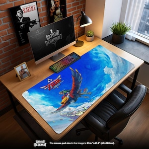 Op de afbeelding: Een grote rechthoekige bureaumat met een levendige illustratie van een vliegend wezen tegen een blauwe lucht. De mat heeft de tekst "ZELDA" en "ARTHUR DESKMAT". De afmeting van de muismat is 60cm x 120cm.
