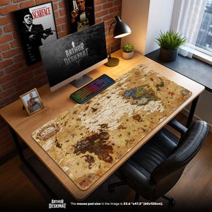 May include: A desk mat with a vintage map design, featuring a distressed, parchment-like appearance. The mat is rectangular and covers a wooden desk, with a computer, keyboard, and lamp visible. The text "ARTHUR DESKMAT" is printed on the mat.