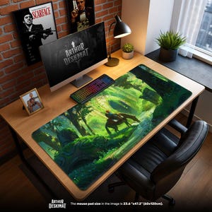 May include: A large rectangular desk mat featuring a vibrant forest scene with a figure on horseback. The mat, measuring 23.6" x 47.2", has the text "ARTHUR DESKMAT" at the bottom. The desk setup includes a computer, keyboard, and framed photos.