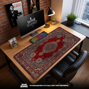May include: A rectangular desk mat with a red and grey oriental rug design. The mat, measuring 60cm x 120cm, features a central medallion and intricate border patterns. The text "ARTHUR DESKMAT" is visible. A computer, keyboard, and desk lamp are on the desk.
