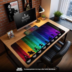 May include: A large rectangular desk mat with a colorful rainbow design and black silhouettes of characters. The mat has the text "ARTHUR DESKMAT" and measures 23.6" x 47.2". The desk mat is on a wooden desk with a computer and keyboard.