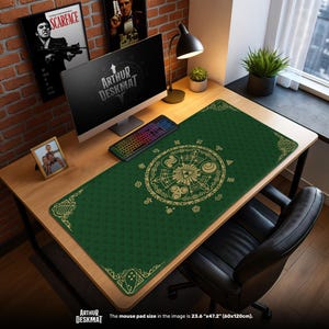 May include: A green desk mat with a gold circular design and the text "ARTHUR DESKMAT". The desk mat is rectangular and measures 23.6" x 47.2". A computer, keyboard, and framed photo are on the wooden desk.