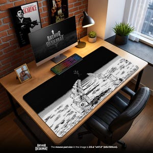 Puede incluir: Alfombrilla de escritorio en blanco y negro con una ilustración de un astronauta en un paisaje lunar. La alfombrilla, de 60cm x 120cm, tiene el texto "ARTHUR DESKMAT". La imagen también muestra un ordenador, un teclado y una lámpara de escritorio.