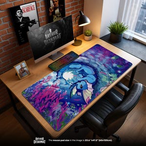 May include: A rectangular mouse mat with an underwater design featuring a blue creature. The mat, measuring 60cm x 120cm, has a dark blue and purple background with pink and green aquatic plants. The text "ARTHUR DESKMAT" is visible.