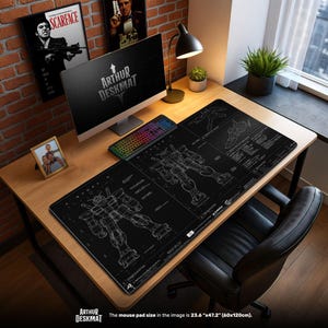 Può includere: Un tappetino per scrivania nero con un disegno di progetto di robot, un computer e una tastiera. Il tappetino misura 60cm x 120cm. Il testo "ARTHUR DESKMAT" è visibile. La scrivania è in legno, con una sedia nera.