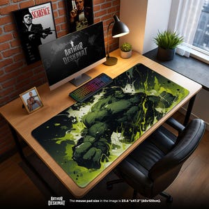 Könnte beinhalten: Eine große Schreibtischunterlage mit einer grün-schwarzen Illustration von Hulk. Das Mauspad ist 60 cm x 120 cm groß. Die Worte "ARTHUR DESKMAT" sind auf der Matte aufgedruckt. Der Schreibtisch hat einen Computer, eine Tastatur und eine Lampe.