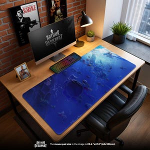 May include: A large blue desk mat with an underwater scene featuring fish and a turtle. The mat, labeled "ARTHUR DESKMAT", measures 23.6" x 47.2". A computer, keyboard, and lamp sit on a wooden desk. Posters and a framed photo are visible.
