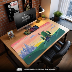 Könnte beinhalten: Rechteckige Schreibtischunterlage mit einer bunten Cartoon-Landschaft, einschließlich Bergen, Bäumen und einem Sonnenuntergang. Die Matte misst 60 cm x 120 cm und trägt den Text "ARTHUR DESKMAT". Ein Computer, eine Tastatur und anderes Schreibtischzubehör befinden sich auf dem Holztisch.