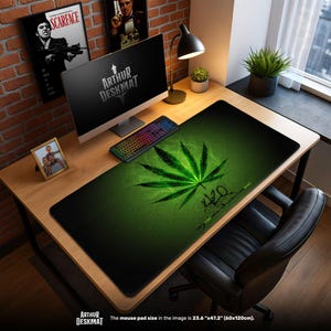 Puede incluir: Una alfombrilla de escritorio negra con un gran diseño de hoja de cannabis verde y el número 420. La alfombrilla es rectangular y está sobre un escritorio de madera, con una computadora, teclado y otros artículos. La alfombrilla mide 60cm x 120cm.