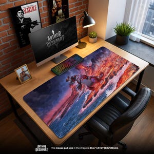 May include: A large rectangular desk mat with a fantasy creature design in red, orange, and blue. The mat, labelled "ARTHUR DESKMAT", measures 60cm x 120cm. A computer, keyboard, and other desk accessories are visible.