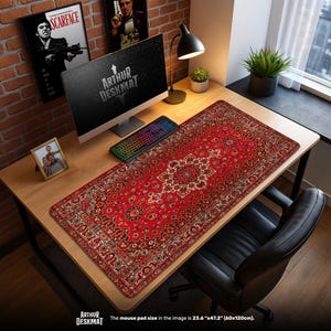 Könnte beinhalten: Eine rot-beige gemusterte Schreibtischunterlage mit Teppichdesign, 60 cm x 120 cm groß. Die Unterlage liegt auf einem Holztisch mit Computer, Tastatur und Lampe. Der Text "ARTHUR DESKMAT" ist sichtbar.