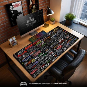 May include: A black desk mat with a collage of band logos and the text "ARTHUR DESKMAT". The mat is 23.6" x 47.2" and sits on a wooden desk with a computer, keyboard, and lamp. The image also includes framed art.