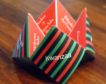 May include: A folded paper decoration with red, black, and green stripes and the word "Kwanzaa" printed on it. The decoration is in the shape of a star or flower, with several triangular sections. Other text is visible.
