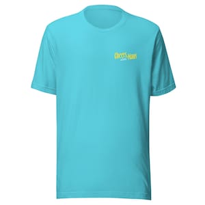 Pode incluir: Uma camiseta turquesa com mangas curtas. A camiseta apresenta o texto "Cheers, Maus" em amarelo na parte superior do peito. A camiseta é feita de um material macio e é adequada para uso casual.