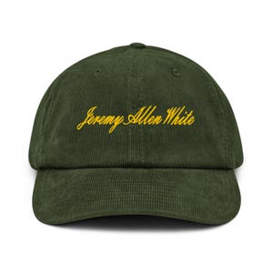 Könnte beinhalten: Dunkelgrüne Cord-Baseballkappe mit dem gestickten Text "Jeremy Allen White" in gelber Schrift. Die Kappe hat einen gebogenen Schirm und eine strukturierte Krone, geeignet für den lässigen Gebrauch.