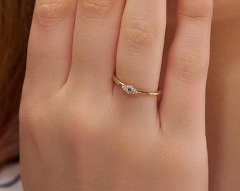 May include: A gold ring with a small, oval-shaped design featuring a blue center stone and surrounding white stones. The ring is delicate and sits on a finger, showcasing its fine details and elegant design.