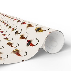 Puede incluir: Un rollo de papel de regalo color crema con un patrón repetido de moscas de pesca coloridas. Las moscas tienen varios colores, incluyendo rojo, marrón y dorado, con anzuelos negros. El papel está enrollado, mostrando el patrón en la superficie.