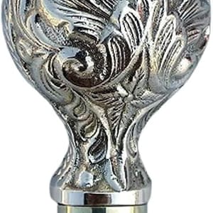 May include: A silver-coloured, ornate walking cane handle. The handle features a detailed, swirling floral design on a rounded top. The base is a cylindrical shape with a brass finish. The overall design is elegant and decorative.